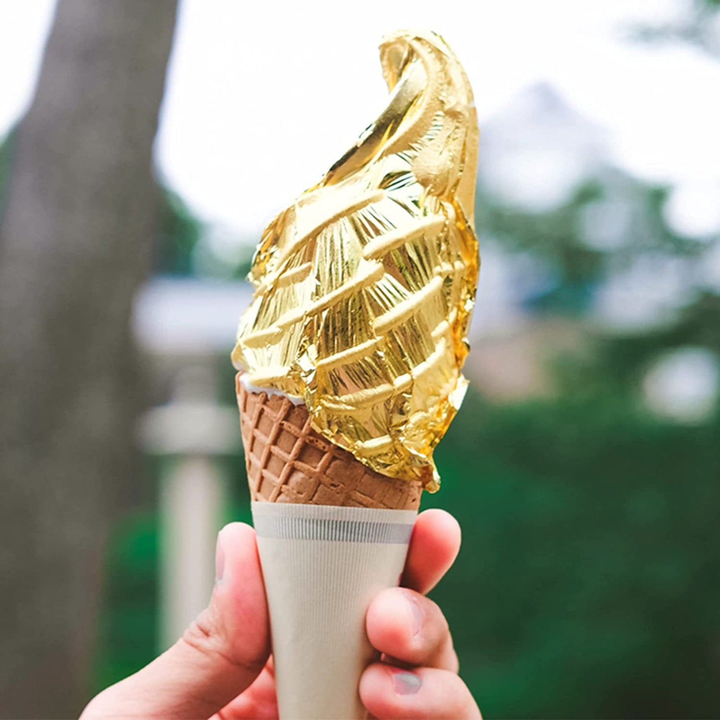 Soft-serve ice cream cone wrapped in edible gold leaf, held in a hand